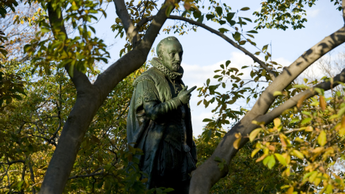 William (Willie) the Silent statue on Voorhees Mall seen through branches and green leaves of a tree.