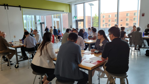 People seated at tables in a bright, modern room with large windows, engaged in conversation during a professional networking event.