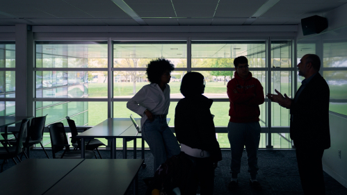 A professor speaking with three students in a classroom