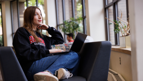 A student sitting in a chair with a laptop looking out the window