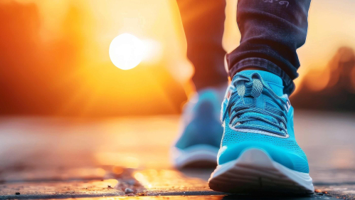 A view of a person's sneakers and shins. The person is walking and the sun is rising behind the person