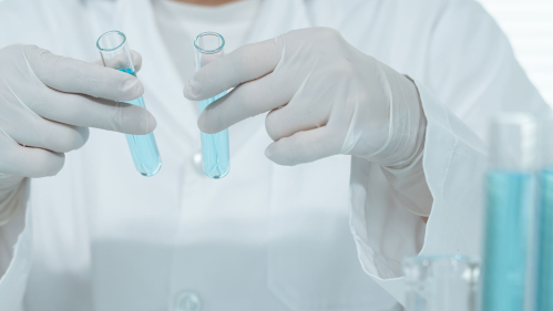 person in white lab coat working with test tubes. only the torso is visible