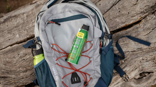 A backpack sitting on a tree trunk. A can of mosquito repellant is placed on top of the back pack.