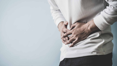 torso of a person in a white shirt clasping hands over stomach, as if in pain
