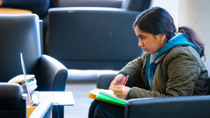 student taking notes while studying on their laptop