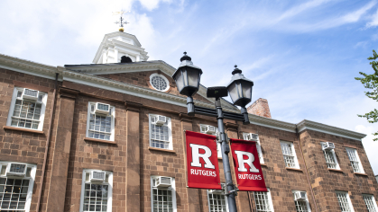 Red Block R banners hang on lamp posts in front of the Old Queens campus on a bright day