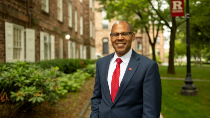 Photo of Provost Geary in front of a Rutgers building and Rutgers flag post