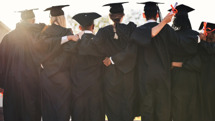 An image of a group of graduates in caps & gowns hugging from behind