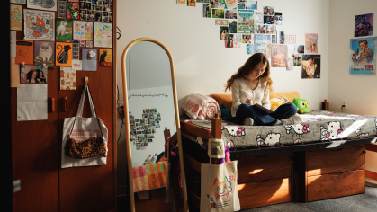 A student sitting on her bed and writing in a dorm room