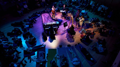 Listeners sitting in a circle around a piano for a performance