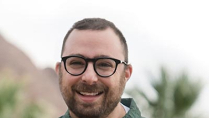 Eric Appell is standing outside wearing a green shirt and smiling at the camera