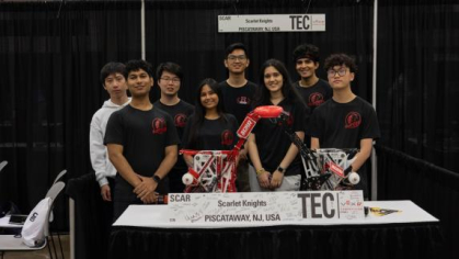 Eight students pose in front of a table with their robotic device