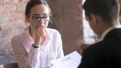 A woman in a pink blouse speaking with a male in a suit that it looking at a resume
