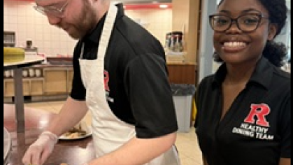 student wearing a chef cap and apron preparing food and another student smiling at the camera in a rutgers healthy dining team polo shirt