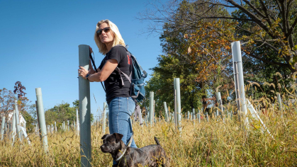 A Rutgers faculty member (with her dog, Poseidon) stands in the floodplain forest she designed in the Watson-Crampton neighborhood of Woodbridge, New Jersey, where houses once stood