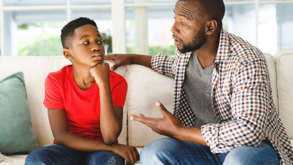 African american son sitting on couch listening to father talking in living room