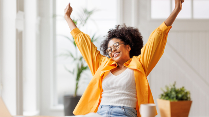 A happy woman putting her hands in the air in front of a laptop