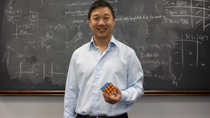 Man standing in front of chalkboard holding Rubik's Cube
