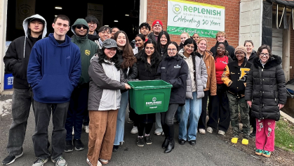 A group of mostly first-year students stand in front of a wall with "Replenish" sign in the back