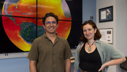 Man and woman standing in front of a poster of the earth and oceans.