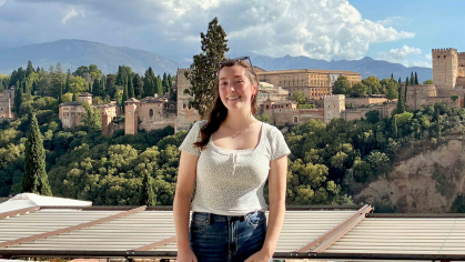 Rutgers graduate Victoria Richard stands before a scenic view of a fortress and palace complex in Spain.