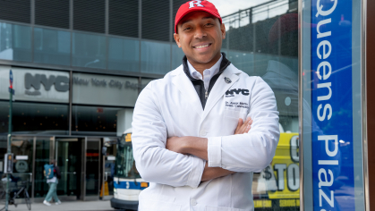 Alumnus Alister Martin wearing a NYC lab coat and a Rutgers Ball cap 