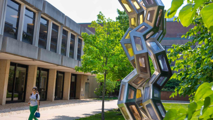 A student walks by the sculpture “Synergy” outside of the Proteomics Building on Busch campus at Rutgers-New Brunswick.