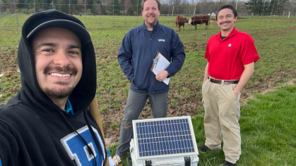 Three scientists stand in a field with a machine