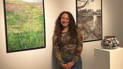 Rutgers graduate Serafina Kennedy poses between two framed works of art in a gallery.