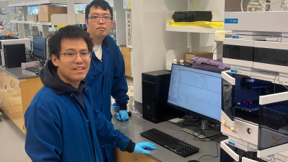 Two men stand in a laboratory before a chemistry research machine.