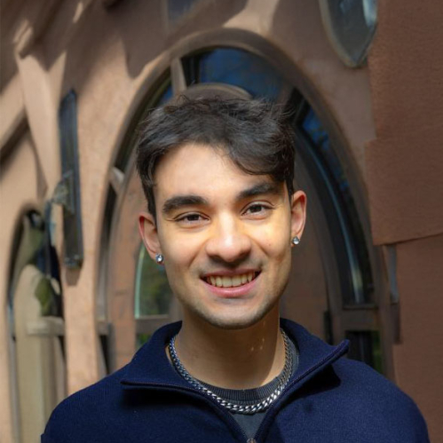 A person wearing a navy blue quarter zip sweater standing in front of a brick facade