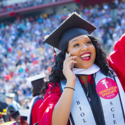 A jubilant graduate with a sticker reading "First Generation Student" on her graduation gown