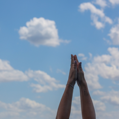 A person doing yoga holds their hands together against a blue sky background