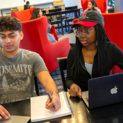 Two students deated at a table in front of laptop computers