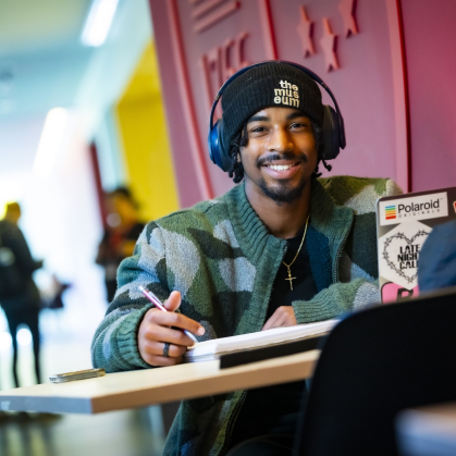 A student smiling and studying while wearing headphones