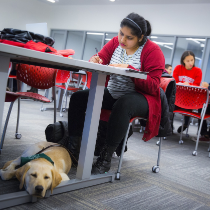 Gayathri Narayanan takes notes in the learning center of the Rutgers Academic Building with her Seeing Eye dog in training