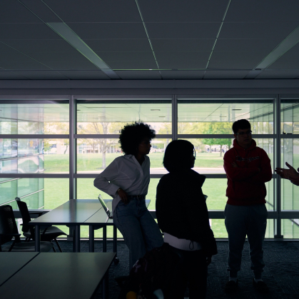 A professor speaking with three students in a classroom