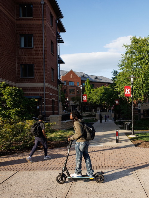 A student riding a scooter around Busch Campus