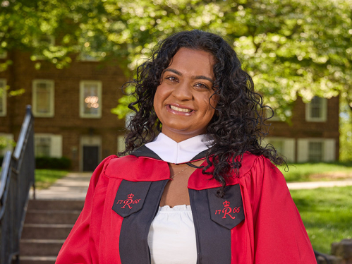 Anjali Vijan standing in front of the Old Queens gate holding her graduation cap.