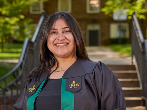 Khushi Kadakia in front of the Old Queens gate holding her graduation cap.
