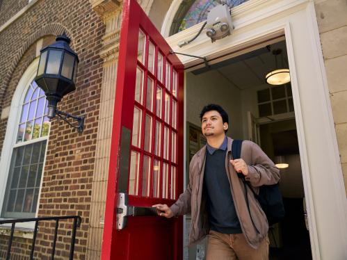 Student, Christopher Godoy, opening a red door exiting Milledoler Hall