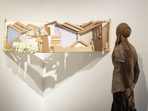 A person looking at a sculpture made of wood, suspended by two walls in a corner