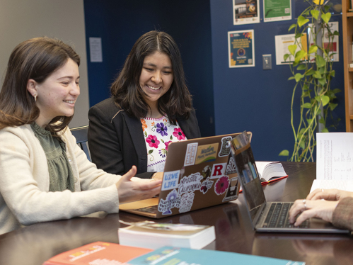 Students sitting at a table working on laptops and smiling