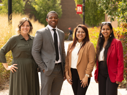 Four working professionals standing on a walkway in front of trees