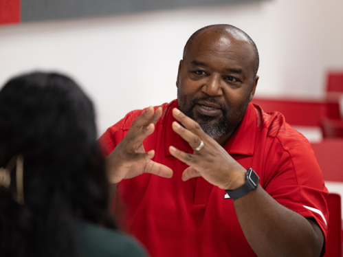 An advisor in a red collared shirt speaking with a student