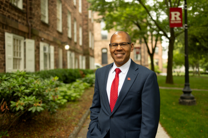 Photo of Provost Geary in front of a Rutgers building and Rutgers flag post