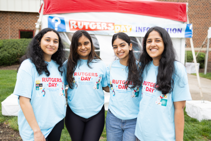 Students wearing Rutgers Day t-shirts standing in front of a Rutgers Day Info Booth