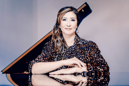 Min Kwon standing at a piano with one arm folded over the other