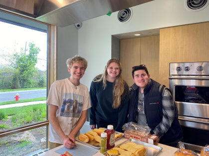 Three students gathered in a kitchen with food for a BBQ