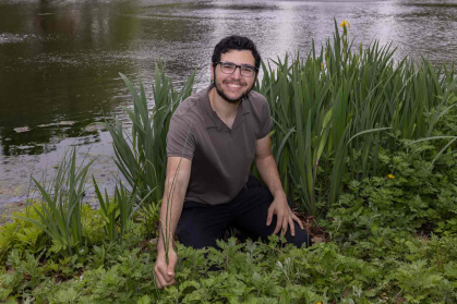Adnan Alkhalili sits and touches grass on the edge of Passion Puddle at Rutgers University-New Brunswick.